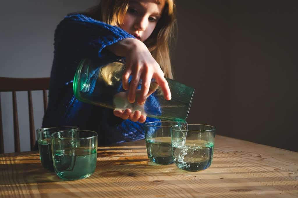 A child pouring water from a jug into a glass