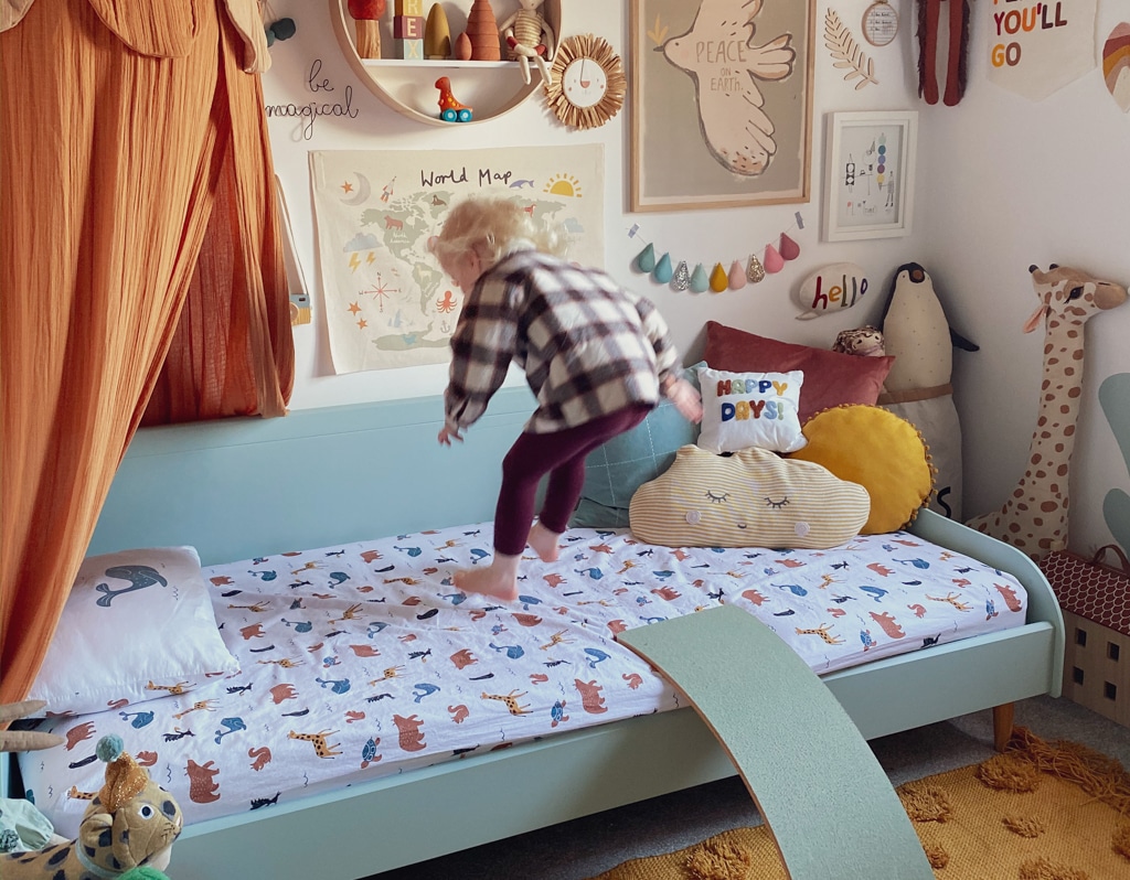 A playful child jumping on a bed in a cozy, colorful bedroom decorated with whimsical wall art, soft toys, and a canopy, showcasing a vibrant and engaging play space.