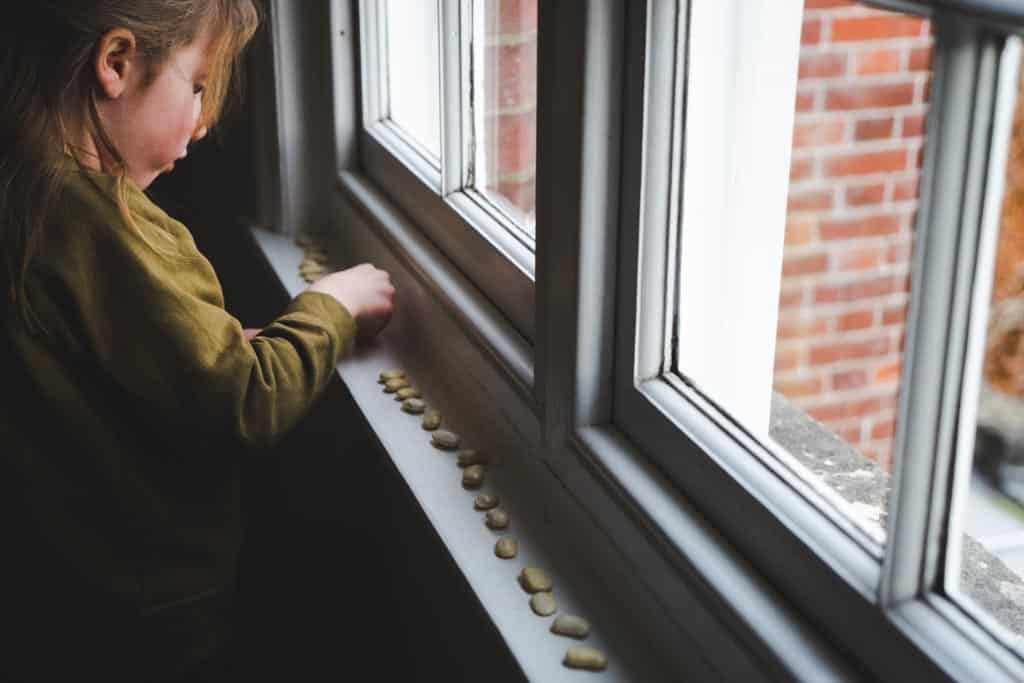 A girl positioning dried beans on windowsill.