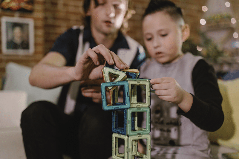 A child and dad building a colorful tower using magnetic tiles