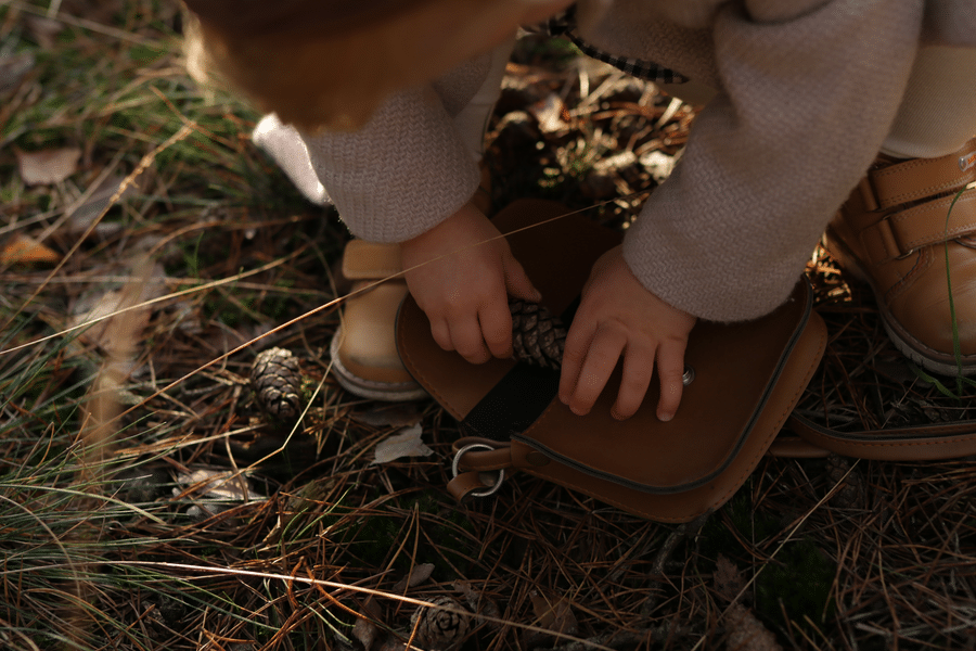 A young child dressed in a beige sweater and brown leather shoes exploring forest